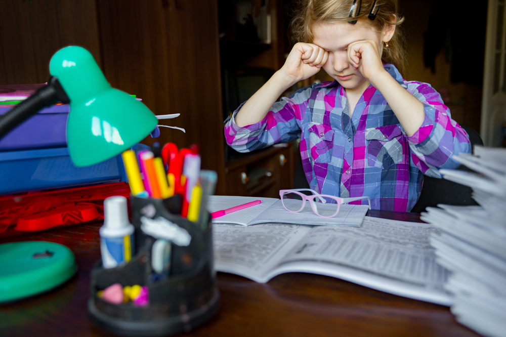 Valokuva, jossa tyttö tekee läksyjä ja hieroo silmiä.