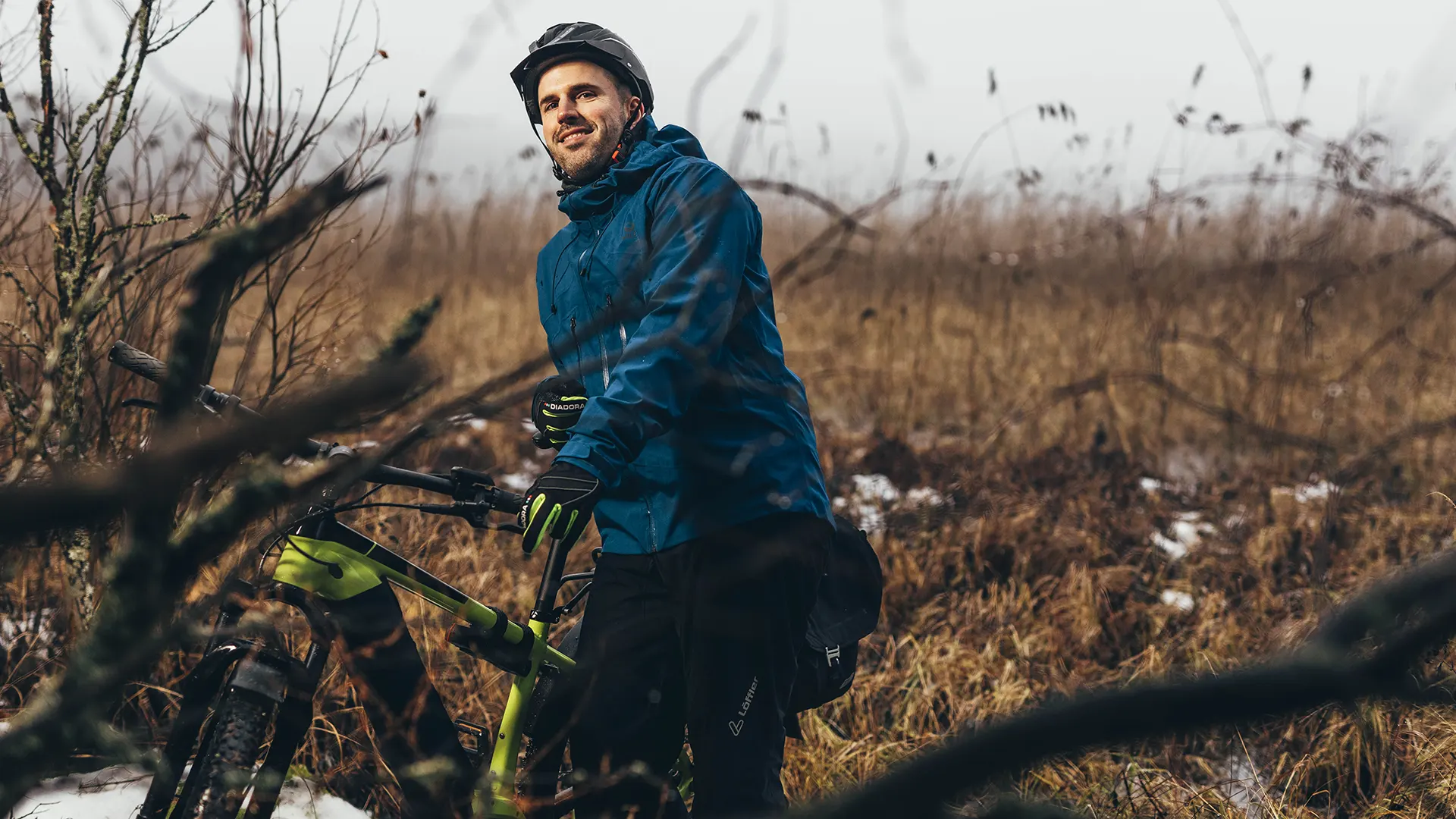 Mies seisoo maastopyöränsä vieressä syksyisessä metsässä.
