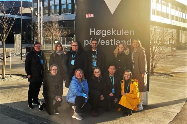 Photo of a group of eleven people in front of the Høgskulen på Vestlandet sign.
