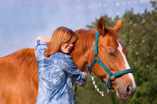 Valokuva, jossa nainen halaa hevosta.