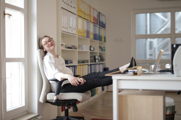 Valokuvassa nainen istuu työpöydän ääressä leväten jalat nostetuna pöydälle.