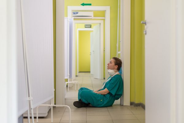 Valokuva sairaanhoitajasta istumassa väsyneen näköisenä käytävällä.